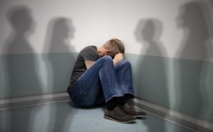 Άτομο καθισμένο σε γωνία, καλύπτει το πρόσωπό του με τα.